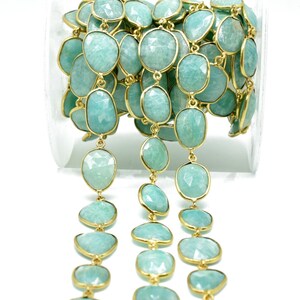May include: A strand of aquamarine gemstone beads with gold-toned accents. The beads are faceted and have a light blue colour. The strand is coiled in a clear container.