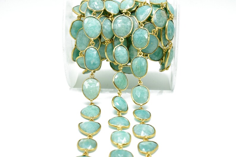 May include: A strand of aquamarine gemstone beads with gold-toned accents. The beads are faceted and have a light blue colour. The strand is coiled in a clear container.