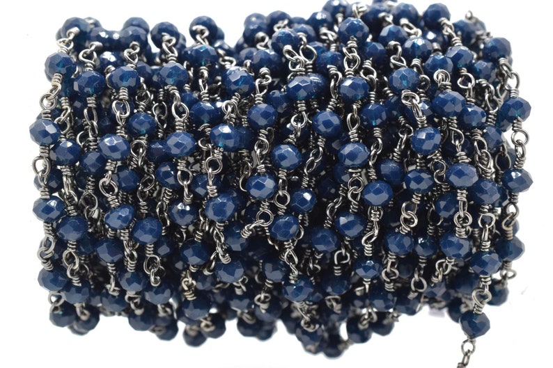 Puede incluir: Primer plano de una cadena hecha de cuentas facetadas de color azul oscuro y eslabones de metal plateado. La cadena est&aacute; enrollada y las cuentas son visibles.