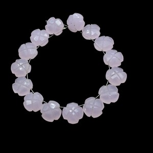 May include: A strand of pale pink gemstone beads, each bead is carved into a flower shape with multiple facets. The beads are strung on a silver wire and form a circle.