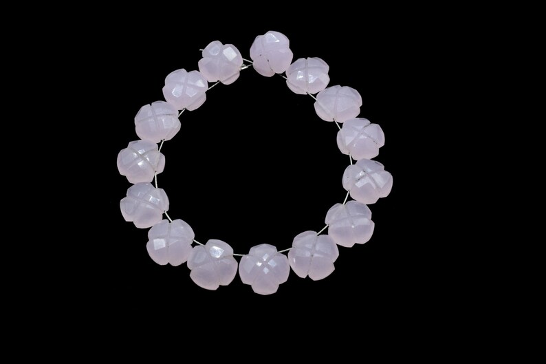 May include: A strand of pale pink gemstone beads, each bead is carved into a flower shape with multiple facets. The beads are strung on a silver wire and form a circle.