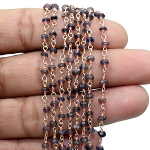 May include: A strand of dark purple gemstone beads strung on a rose gold chain. The beads are faceted and have a slightly irregular shape.