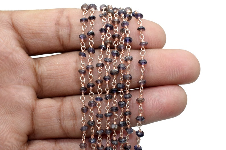 May include: A strand of dark purple gemstone beads strung on a rose gold chain. The beads are faceted and have a slightly irregular shape.