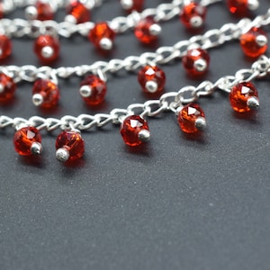 May include: A silver chain necklace with multiple strands and red crystal beads. The beads dangle from the chain and are faceted.