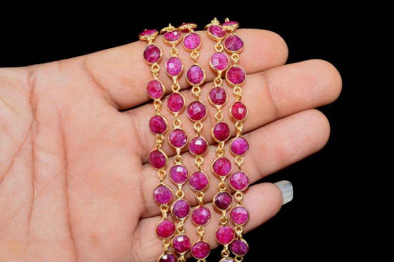 May include: A strand of ruby gemstone beads strung on a gold chain. The beads are faceted and have a deep red colour.