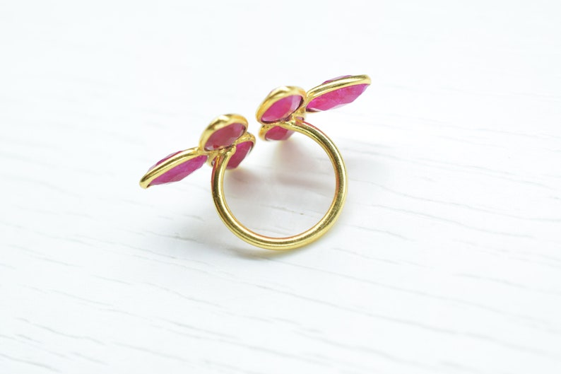 Peut inclure: Une bague en or avec trois accents de pierres pr&eacute;cieuses roses. La bague est ouverte et les pierres pr&eacute;cieuses sont dispos&eacute;es en forme de fleur.