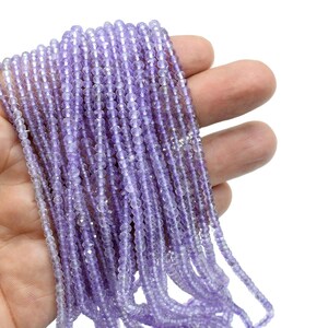 May include: A strand of light purple amethyst beads, approximately 4mm in diameter, with a faceted finish. The beads are strung on a clear thread and are displayed in a hand.
