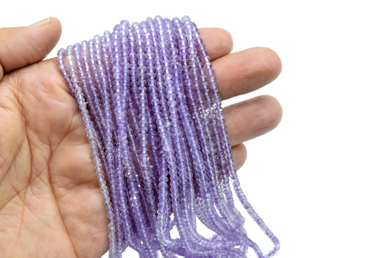 May include: A strand of light purple amethyst beads, approximately 4mm in diameter, with a faceted finish. The beads are strung on a clear thread and are displayed in a hand.
