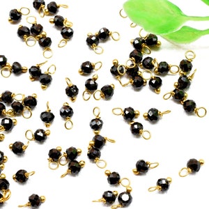 Puede incluir: Una dispersión de cuentas facetadas negras con anillos de salto dorados, perfectas para la elaboración de joyas.