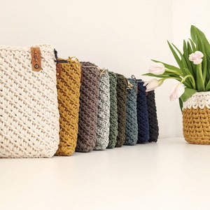 May include: A row of crocheted bags in various colors, including white, yellow, green, and blue. The bags are lined up on a white surface. The bags are made with a simple stitch pattern and have a leather strap.