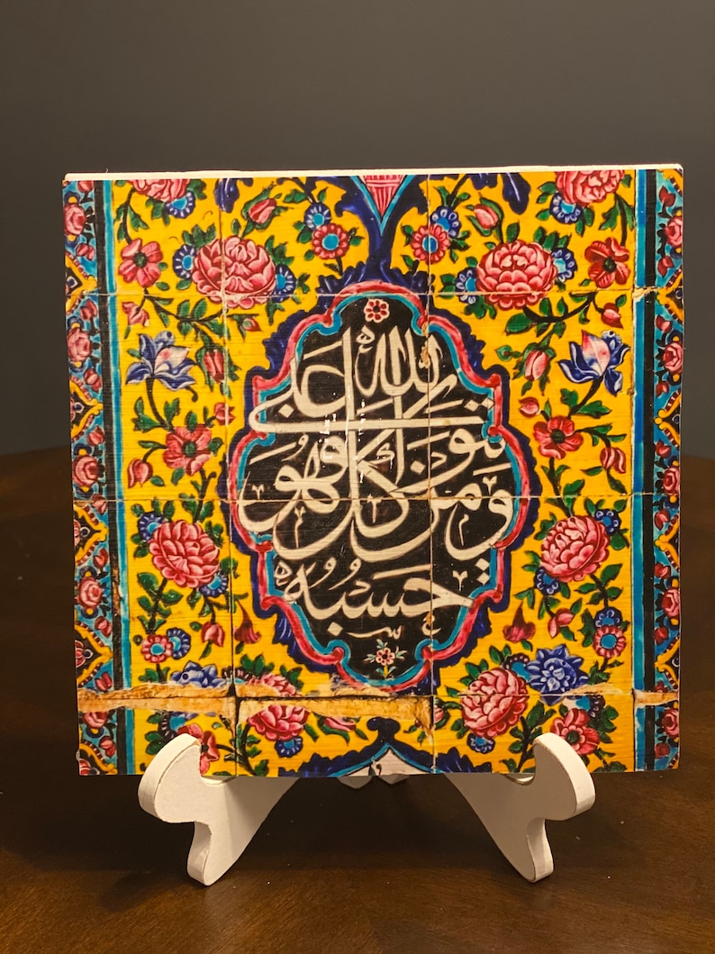 May include: A colorful ceramic tile with intricate floral patterns and Arabic calligraphy in black. The tile is mounted on a white easel.