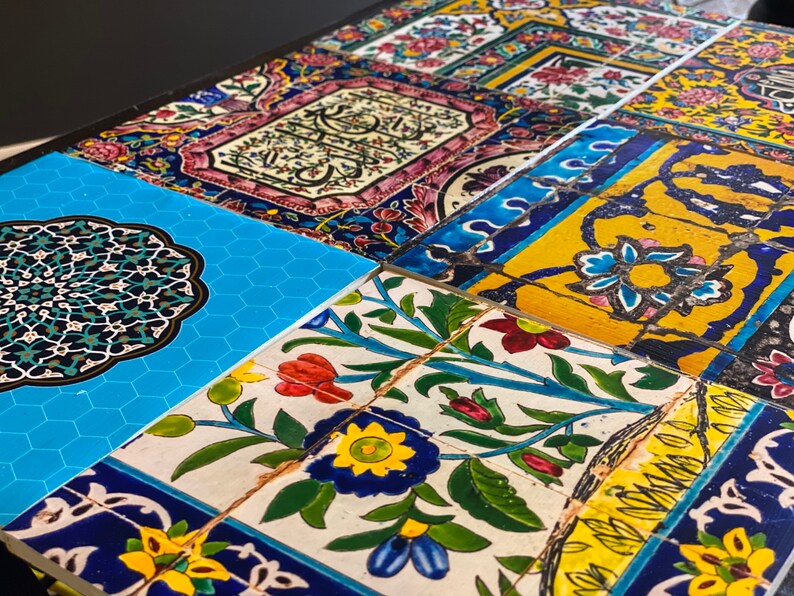 May include: A close-up of a table top covered in colorful, patterned tiles. The tiles feature floral designs, geometric shapes, and Arabic script. The tiles are arranged in a patchwork pattern.