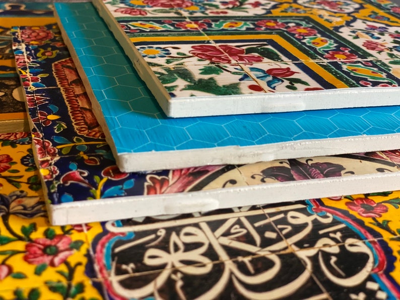May include: Close-up of the edges of three ceramic tiles with intricate floral patterns and Arabic calligraphy. The tiles are stacked on top of each other, with the top tile featuring a blue and white geometric pattern.