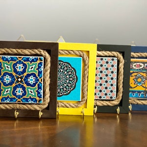 May include: Four keychains with different patterned tiles framed in wood and rope. The frames are painted in black, yellow, black, and blue.