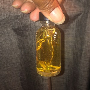 Puede incluir: Una pequeña botella de vidrio con tapa negra llena de un líquido amarillo y que contiene pequeños trozos de hierbas secas.