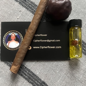 May include: A business card with the name "Cipherflower" and the website "www.Cipherflower.com" printed on it. A brown cigar, a dark brown fruit, and a small clear glass bottle with yellow liquid are on the card.
