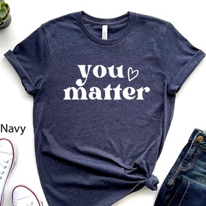 Könnte beinhalten: Ein heidefarbenes marineblaues T-Shirt mit dem Text "you matter" in Weiß mit einem kleinen Herzsymbol.