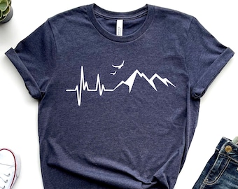 Könnte beinhalten: Ein marineblaues T-Shirt mit einer weißen Grafik einer Bergkette und einem Herzschlag mit Vögeln, die über den Bergen fliegen.