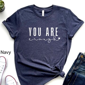 Könnte beinhalten: Ein heidefarbenes marineblaues T-Shirt mit dem Text "YOU ARE enough" in weißen Buchstaben und einem kleinen Herz.