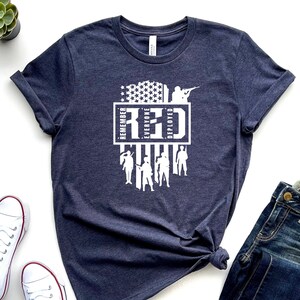 Könnte beinhalten: Ein marineblaues T-Shirt mit einem weißen Grafikdesign. Die Grafik zeigt eine stilisierte amerikanische Flagge mit den Worten "Remember Everyone Deployed" und dem Akronym "RED".
