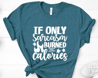 Puede incluir: Una camiseta azul turquesa con el texto "IF ONLY sarcasm BURNED calories" en blanco. La camiseta está anudada y se encuentra sobre una superficie de madera blanca.