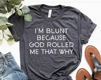 May include: A dark gray t-shirt with the text "I'm blunt because God rolled me that why" printed in white.