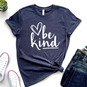 May include: A navy blue t-shirt with a white heart and the text "be kind" in a white, handwritten font.