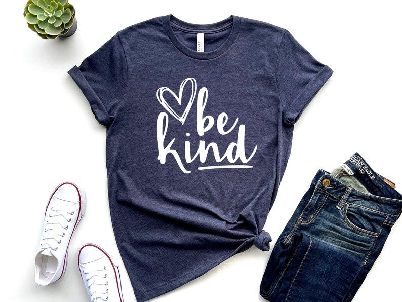 May include: A navy blue t-shirt with a white heart and the text "be kind" in a white, handwritten font.