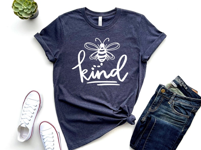 May include: A navy blue t-shirt with a white bee graphic and the word "kind" written in white cursive lettering.