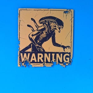 May include: A distressed yellow sign featuring a black illustration of an Alien creature and the word "WARNING". The sign has a weathered appearance with torn edges, suggesting a vintage aesthetic. The background is a solid blue.