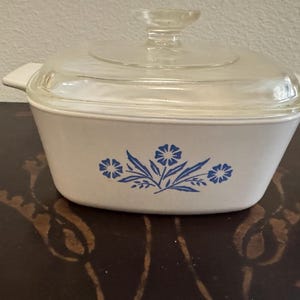 Könnte beinhalten: Weiße Keramik-Backform mit Glasdeckel. Die Form hat ein blaues Blumenmuster mit einem Muster aus blauen und weißen Blumen.