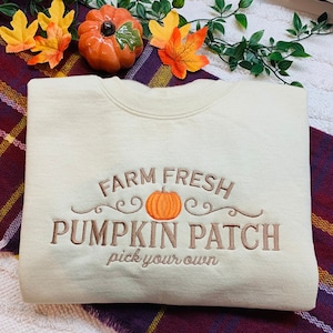 May include: A light beige sweatshirt with the text "Farm Fresh Pumpkin Patch pick your own" embroidered in brown. A small orange pumpkin is embroidered in the centre of the text.