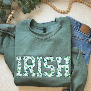May include: Green sweatshirt with the word "IRISH" in white letters outlined in black. The letters are filled with a pattern of green shamrocks.