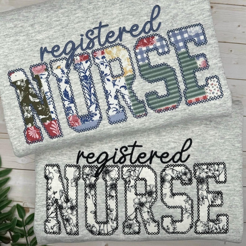 May include: Two grey sweatshirts with the words "registered NURSE" in decorative lettering. One shirt features patchwork letters with floral and patterned fabrics. The other shirt has black floral designs within the letters.