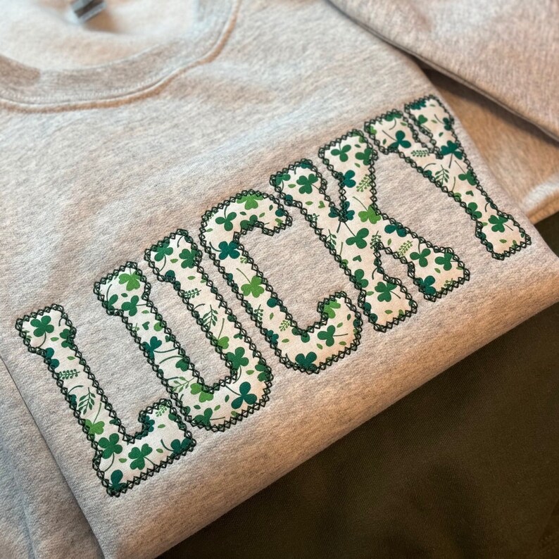 May include: A gray sweatshirt with the word "LUCKY" embroidered in green shamrock-patterned fabric.