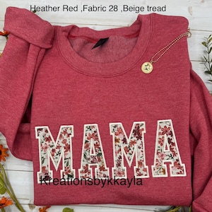 May include: Heather red sweatshirt with the word "MAMA" in large, floral-filled letters. A gold necklace with a pendant rests on the shirt. The text "Kreationsbykkayla" is at the bottom.