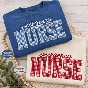 May include: A heather blue sweatshirt with the text emergency NURSE in blue and white gingham, and a cream sweatshirt with the text emergency NURSE in red and white gingham. Both feature a crew neckline and long sleeves with a textured fabric finish.