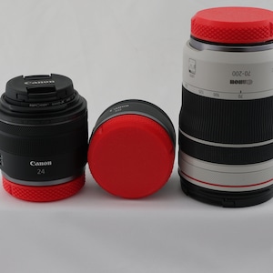 May include: Three camera lenses with red lens caps. The lens on the left is a Canon 24mm lens. The lens in the middle is a Canon lens with a red lens cap. The lens on the right is a Canon 70-200mm lens.