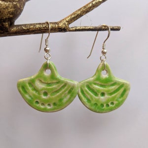 May include: A pair of green ceramic earrings with a fan-shaped design. The earrings are on a silver hook.