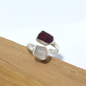 May include: A silver ring with a red and white gemstone setting. The ring is designed to wrap around the finger.