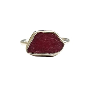Puede incluir: Un anillo de plata con una gran piedra preciosa roja irregular engastada en el centro.