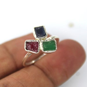 以下が含まれることがあります： 赤、緑、青の正方形の宝石が3つ付いたシルバーリング。 宝石はクラスターデザインで、シンプルなバンドが付いています。 リングは白い背景に表示されています。