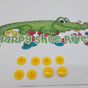 May include: Eight yellow plastic shoe rivets with a small post on the top. The rivets are arranged in two rows of four. The image also includes a cartoon alligator with the text "snappy shoe rivets" below it.