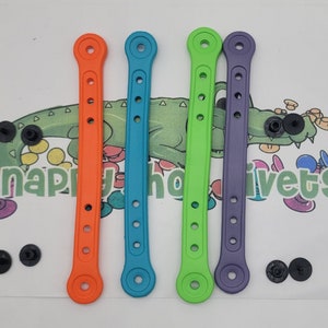May include: Four colorful rubber straps with a round hole at each end. The straps are orange, blue, green, and purple. The straps are about 2 inches long.