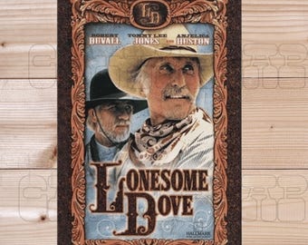 May include: A framed DVD cover for the movie "Lonesome Dove" featuring Robert Duvall, Tommy Lee Jones, and Angelica Huston. The artwork has a vintage western theme with a brown border and the title in large, stylized letters. The DVD contains the entire 6 hours of Lonesome Dove on one DVD.