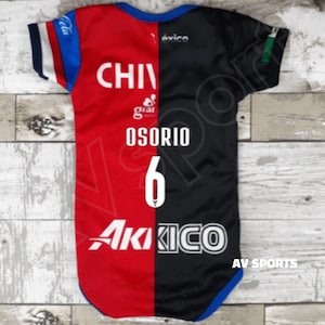 May include: A red and black soccer jersey with the text "CHIVAS" and "OSORIO 6" on the back. The jersey has a white logo on the front and the text "AKIKO" on the bottom.