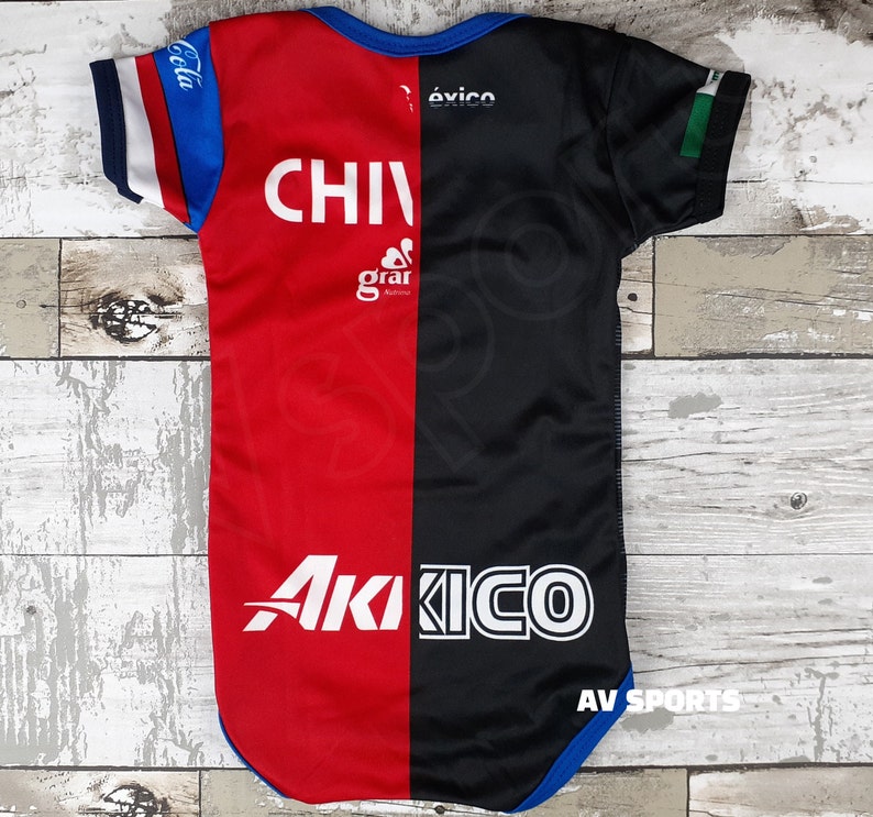 May include: Red and black baby bodysuit with the text "CHIVAS" and "Akiko" in white. The bodysuit has blue trim and the text "Coca Cola" and "&eacute;xico" on the sleeves.