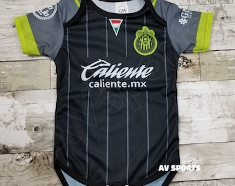 May include: Black and green baby onesie with a soccer team logo and the text "Caliente caliente.mx".