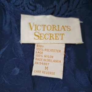K&ouml;nnte beinhalten: Ein wei&szlig;es Etikett mit schwarzem Text, auf dem "VICTORIA'S SECRET" steht und die Stoffzusammensetzung als 100% Polyester f&uuml;r den K&ouml;rper und 100% Nylon f&uuml;r die Spitze angegeben ist. Das Etikett tr&auml;gt au&szlig;erdem die Aufschrift "MADE IN SRI LANKA" und "RN 54867". Das Etikett hat die Gr&ouml;&szlig;e "M" und die Aufschrift "CARE REVERSE".