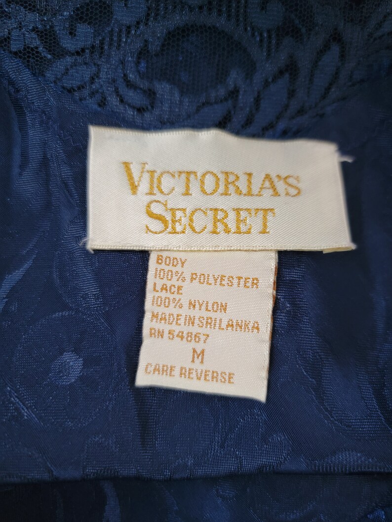 K&ouml;nnte beinhalten: Ein wei&szlig;es Etikett mit schwarzem Text, auf dem "VICTORIA'S SECRET" steht und die Stoffzusammensetzung als 100% Polyester f&uuml;r den K&ouml;rper und 100% Nylon f&uuml;r die Spitze angegeben ist. Das Etikett tr&auml;gt au&szlig;erdem die Aufschrift "MADE IN SRI LANKA" und "RN 54867". Das Etikett hat die Gr&ouml;&szlig;e "M" und die Aufschrift "CARE REVERSE".